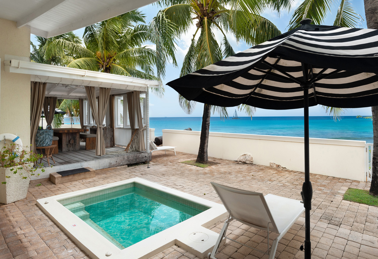 Striped umbrella, plunge pool and Caribbean sea at beachfront Barbados villa Little Good Harbour House.